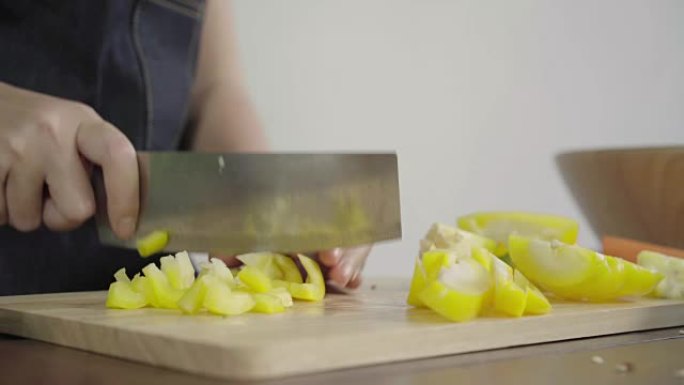 首席女士制作沙拉健康食品并在砧板上切碎甜椒的特写镜头。