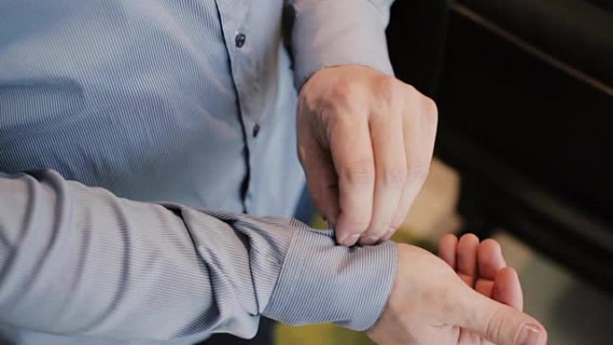 男性手扣上衬衫的特写视图。男人紧扣衬衫上的袖口。商人准备工作