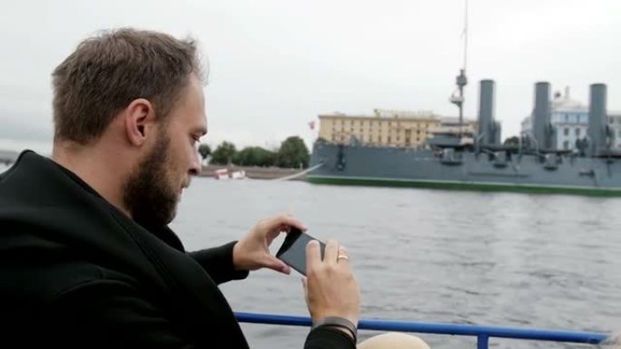 一个人在观光。使用智能手机，backview，慢速mo拍摄圣彼得堡的巡洋舰Aurora的照片