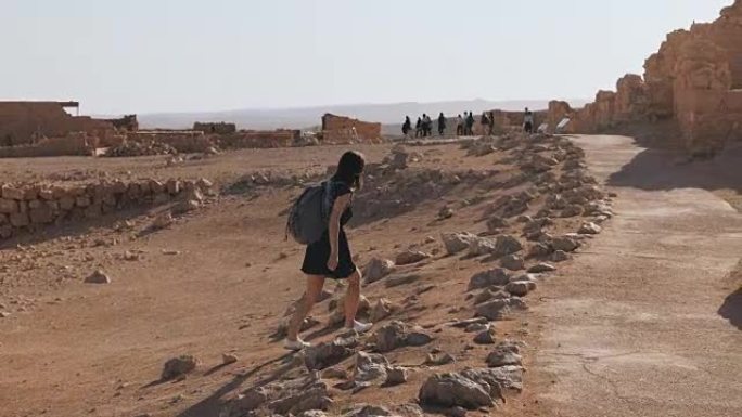 背着背包的女孩探索沙漠废墟。漂亮的欧洲女性旅行者走在古老的风景中。马萨达以色列4K