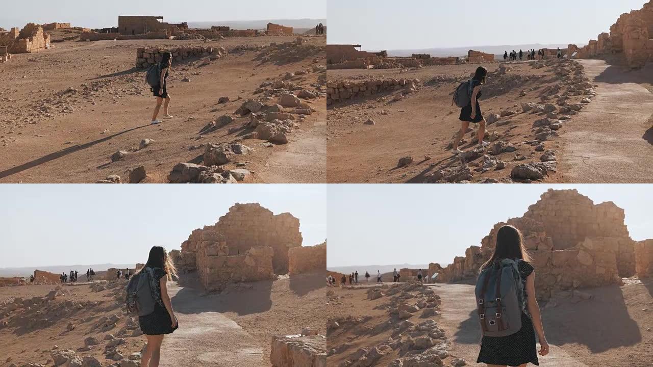 背着背包的女孩探索沙漠废墟。漂亮的欧洲女性旅行者走在古老的风景中。马萨达以色列4K
