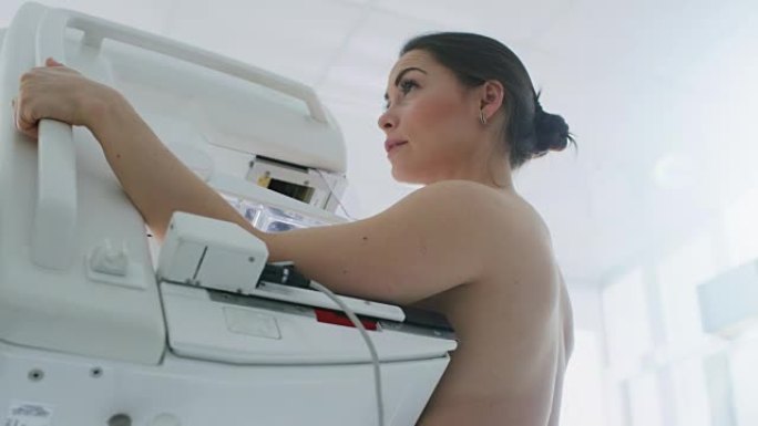 在医院，低角度肖像拍摄的半裸女性病人进行乳房x线筛查程序。健康年轻女性进行癌症预防性乳房x线摄影扫描