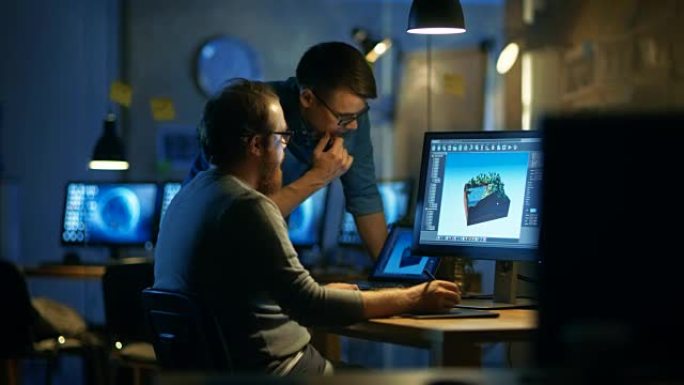 两个男性游戏开发者讨论游戏关卡绘制，一个使用图形平板电脑。他们在阁楼办公室工作到很晚。