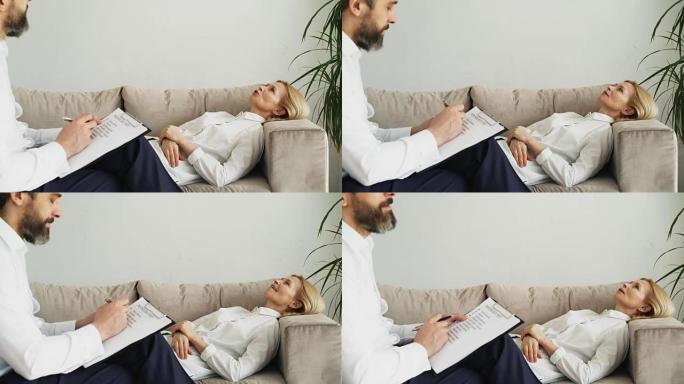 成年妇女躺在沙发上，在办公室里与专业的男性心理治疗师或心理学家谈论自己的问题