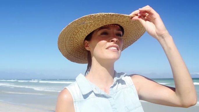 美丽的女人在海滩散步时戴着帽子