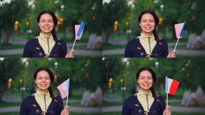 迷人女孩的慢动作肖像法国体育迷手持法国国旗，微笑着看着相机。活跃的女性，美丽的自然和国家观念。