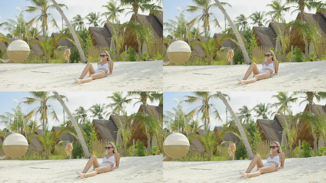 美丽的金发女人躺在沙滩上。在背景蔚蓝的海洋和白色的沙子。地球上的天堂。