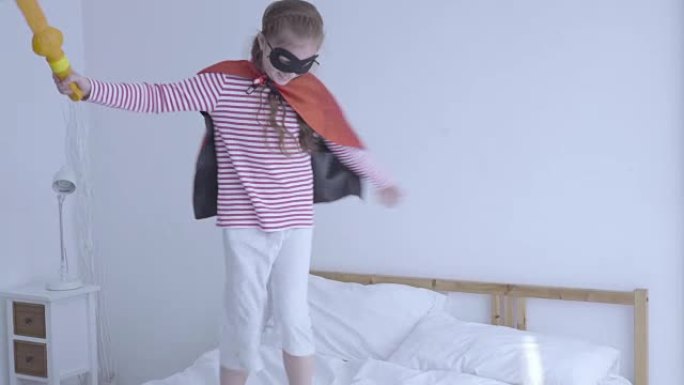 儿童女孩角色扮演英雄在床上跳跃。