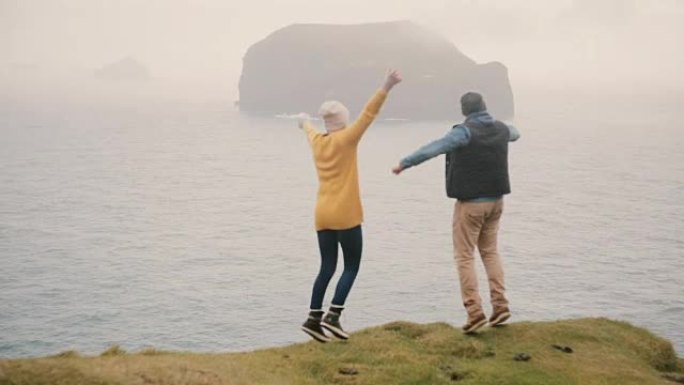 年轻幸福的夫妇站在悬崖边欢快地跳跃。游客男女在海边拥抱