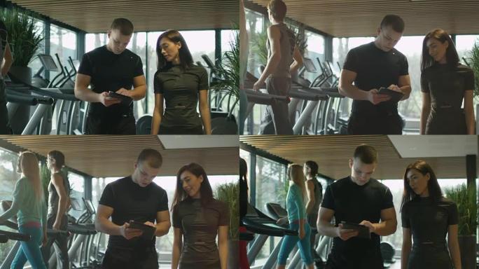 运动中的男人和女人在健身房的跑步机旁使用平板电脑。