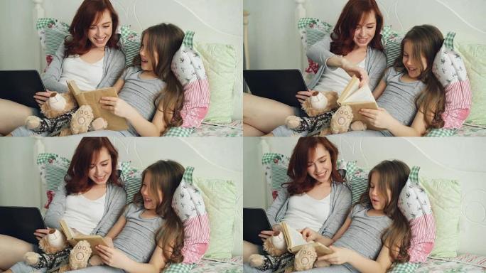 可爱的小女儿和年轻的慈爱的母亲看着有趣的图片，一边笑着一边看童话书，一起坐在家里舒适的床上