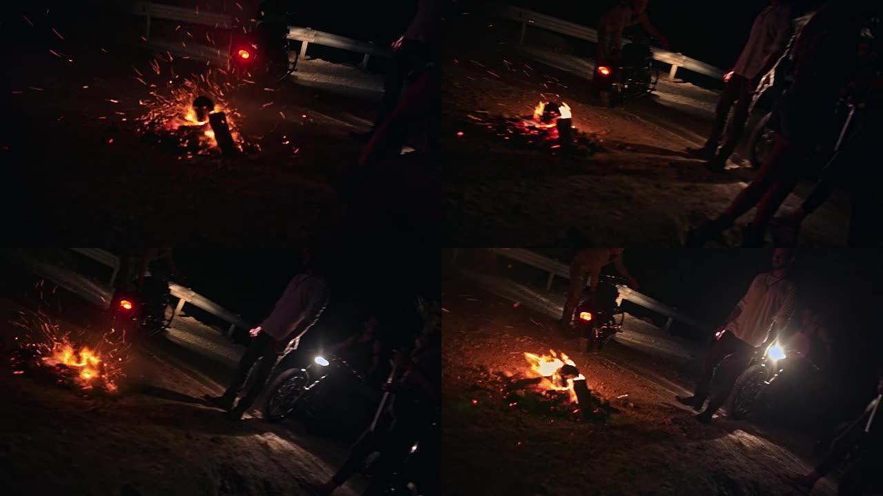 年轻的反叛摩托车手朋友晚上站在篝火旁