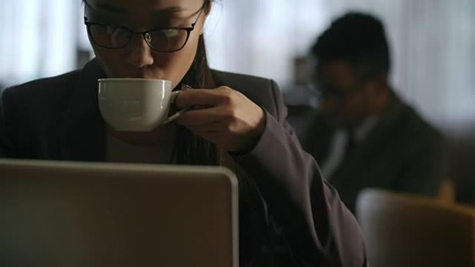亚洲妇女在笔记本电脑上，在酒店大堂喝咖啡