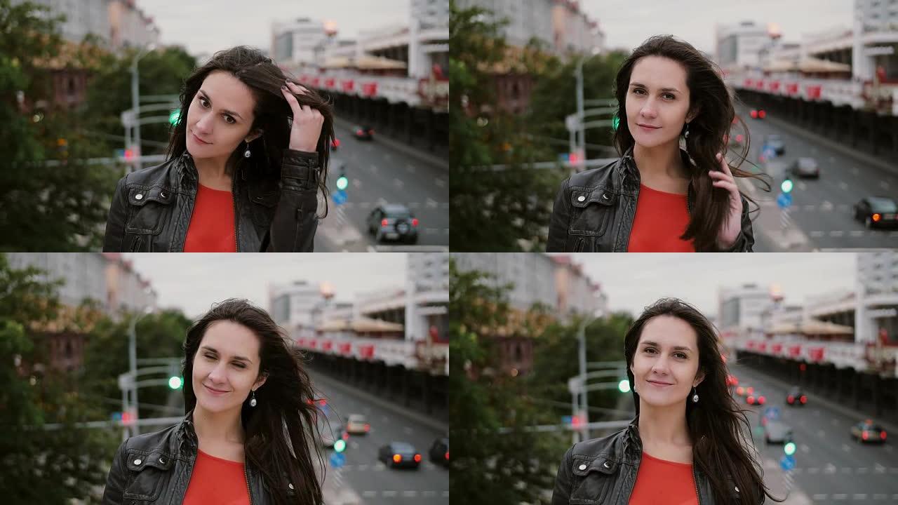 微笑的美丽女孩站在桥上，抚摸她的头发，看着镜头。风吹她的长发。全高清