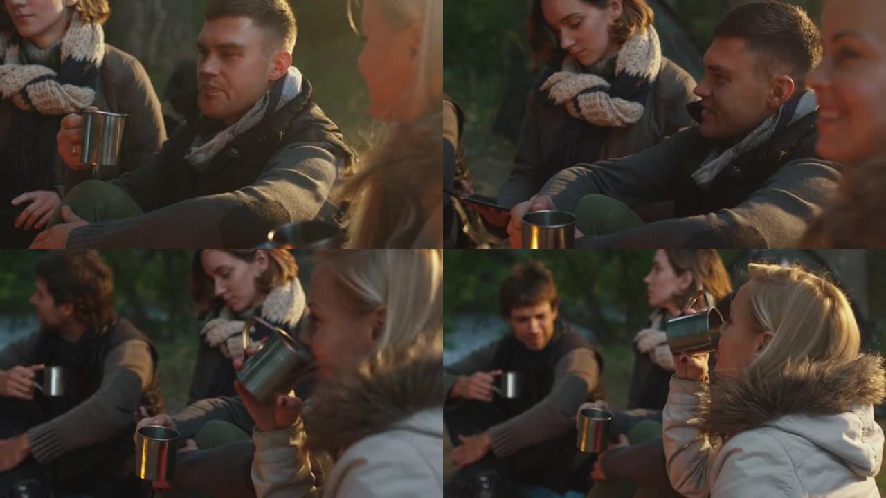 一群朋友坐在篝火旁的森林里，用热水瓶里的热饮聊天。
