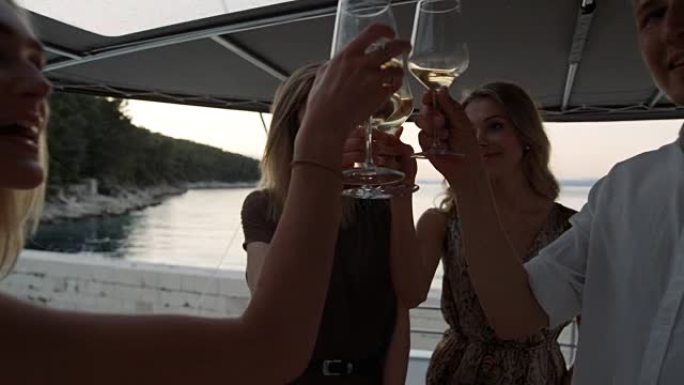 快乐的年轻男女在游艇上庆祝，他们碰杯香槟酒并敬酒。美丽的自然和海滨景色。
