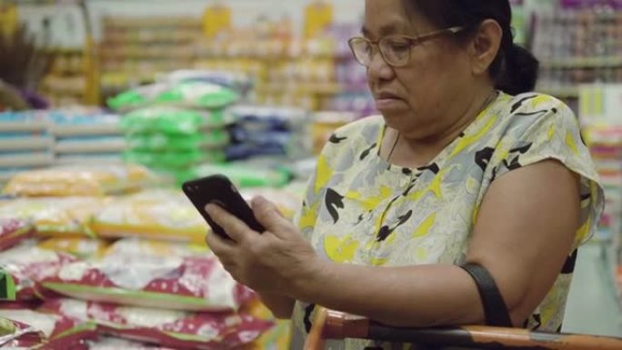 在超市使用智能手机的亚洲高级女性