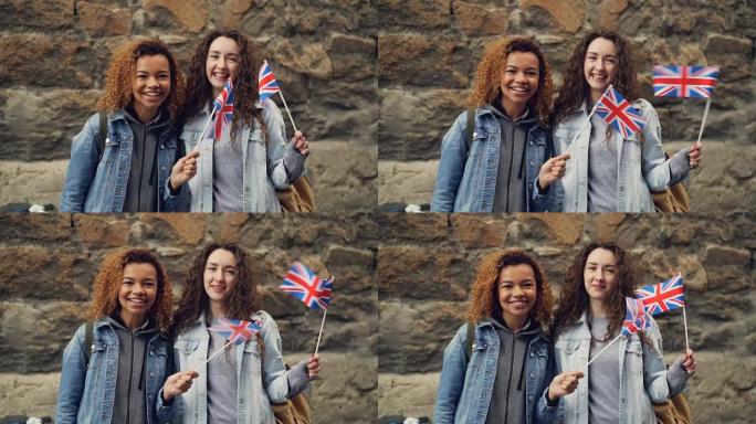 两名女性朋友的Slowmotion肖像英国留学生挥舞着英国国旗，笑着看着相机。友谊、旅游和幸福的人的