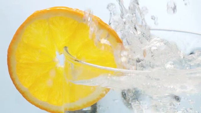 冰块掉落在用橙色切片装饰的水玻璃中