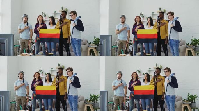 多民族的朋友在家里一起听和唱德国国歌，然后一起看电视上的体育锦标赛