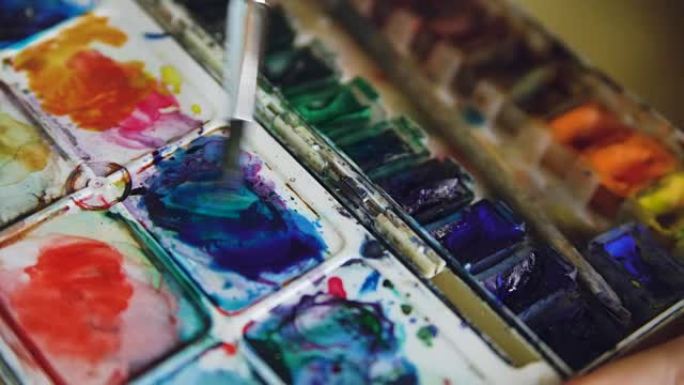 年轻的女艺术家用水彩画画画。特写画笔在托盘中混合颜色