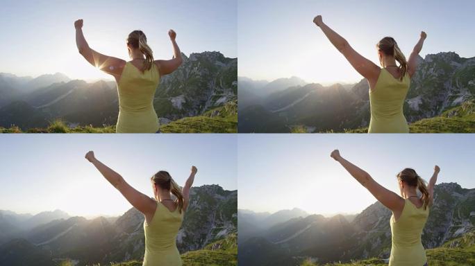 慢动作年轻女徒步旅行者抬起手臂凝视山顶上的日落