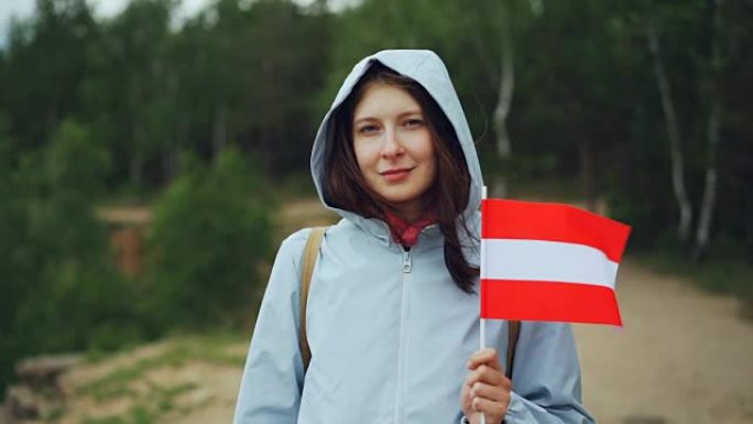 美丽的奥地利女士骄傲的公民手持拉脱维亚国旗，微笑着看着相机的慢动作肖像。国籍，环游世界和人们的观念。