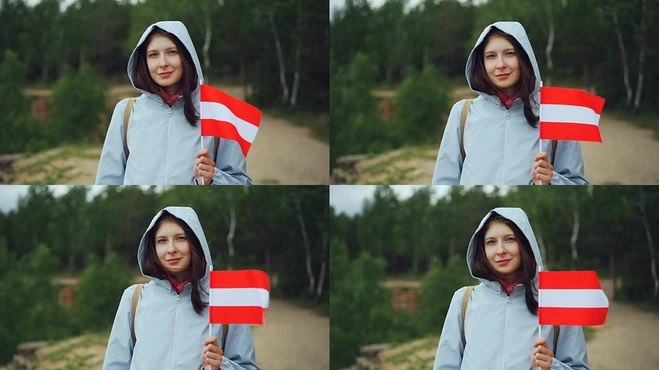 美丽的奥地利女士骄傲的公民手持拉脱维亚国旗，微笑着看着相机的慢动作肖像。国籍，环游世界和人们的观念。