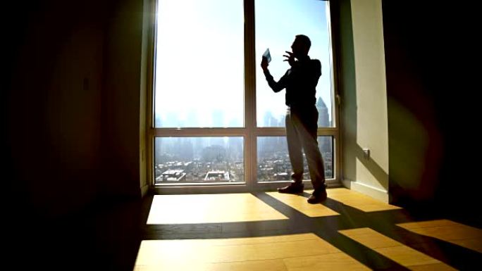 男人在大窗户上打开百叶窗的轮廓。阳光照进房间，产生阴影。
