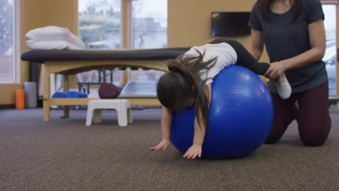 年轻的女孩躺在健身球上，而理疗师则握住她的腿