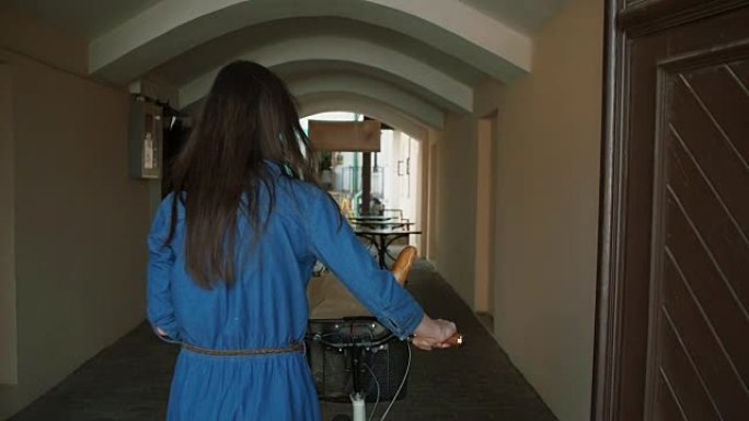 一个长发的黑发女孩骑着自行车走进老城区的老门，慢镜头，斯蒂德卡姆镜头