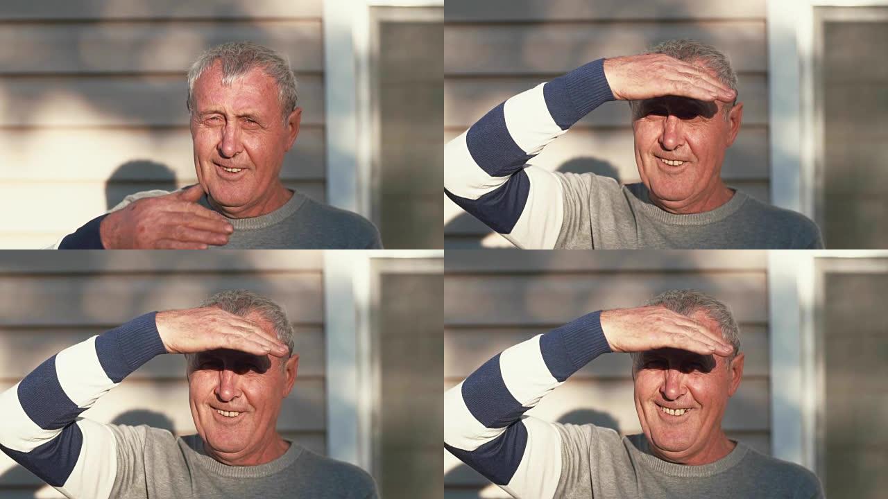 一位老人看着相机，遮住阳光，微笑着。慢mo