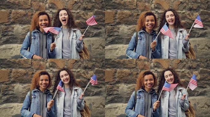 两个朋友的慢动作肖像，穿着便服的年轻女性挥舞着美国国旗，笑着看着相机。友谊、旅游和幸福的人的概念。