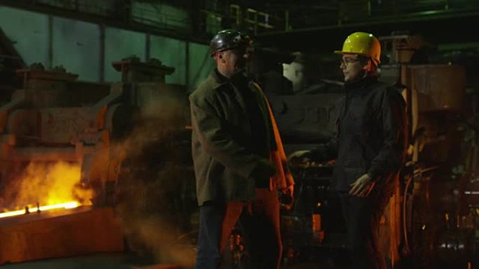 工程师和工人在铸造厂交谈。恶劣的工业环境。