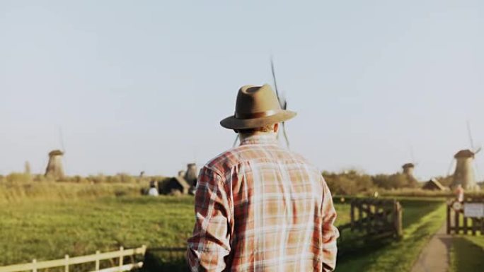 4k成功欧洲农民男性肖像。穿着衬衫和帽子的男人，带着智能手机和智能手表走向磨坊