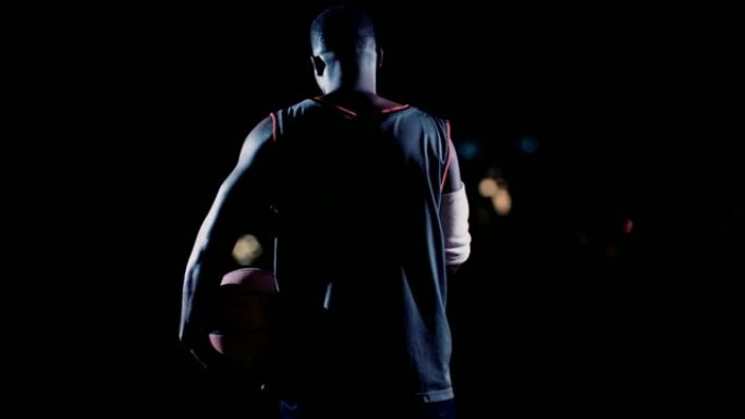 篮球运动员在夜间将篮球放在臀部