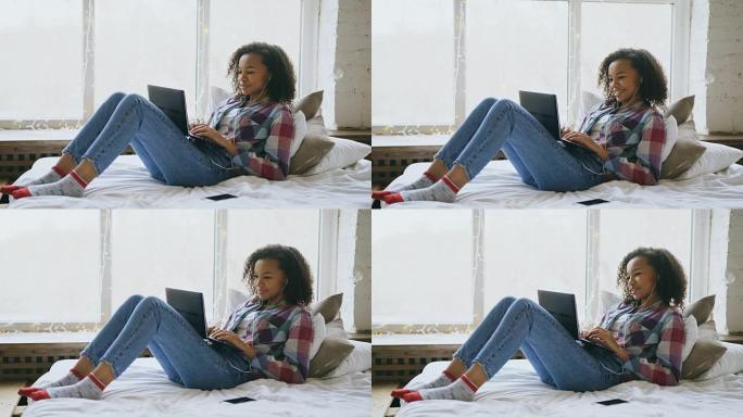 快乐的混血女孩躺在床上用笔记本电脑和朋友视频聊天