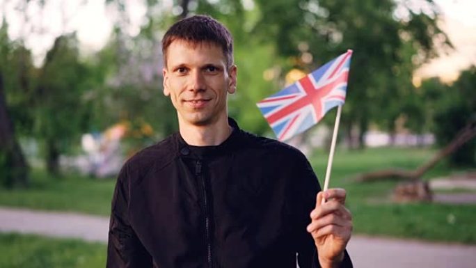 慢动作的肖像快乐的英国人骄傲的公民挥舞着英国的官方旗帜，看着镜头和微笑。人与国家符号概念。