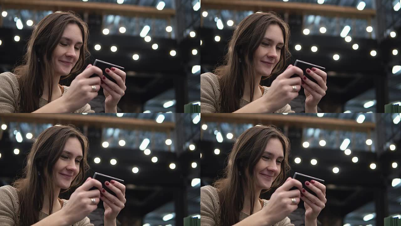 特写肖像。女人在背景4k的现代咖啡厅灯光中使用她的smartphon触摸屏设备