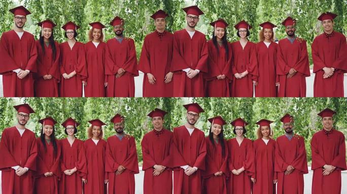 站在户外的多种族毕业学生的肖像穿着红色礼服和灰泥板，微笑着看着相机。