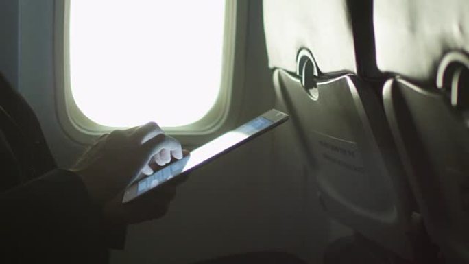 特写镜头中的年轻人正在窗户旁边的飞机上使用平板电脑。