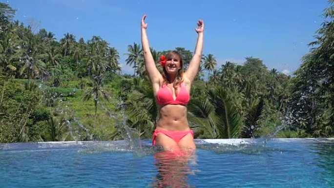 特写微笑的女孩在热带岛屿的无边泳池里溅水滴