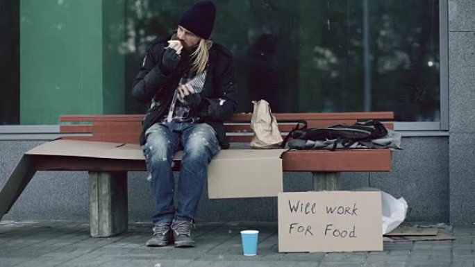 由于美国移民危机，无家可归和失业的美国男子在城市街道的长凳上吃三明治