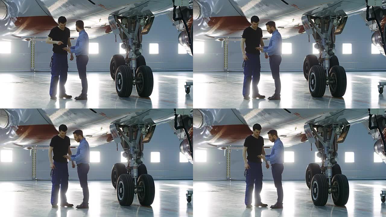 在机库，飞机维修工程师向飞机技术员展示平板电脑上的技术数据。他们站在干净的新飞机旁边。