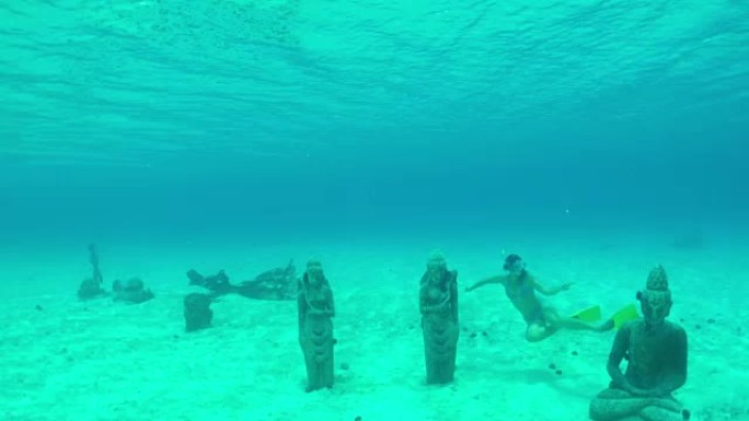 水下特写: 年轻女子在水面下游泳，在清澈的绿松石蓝色泻湖中发现沉没的佛像保护区