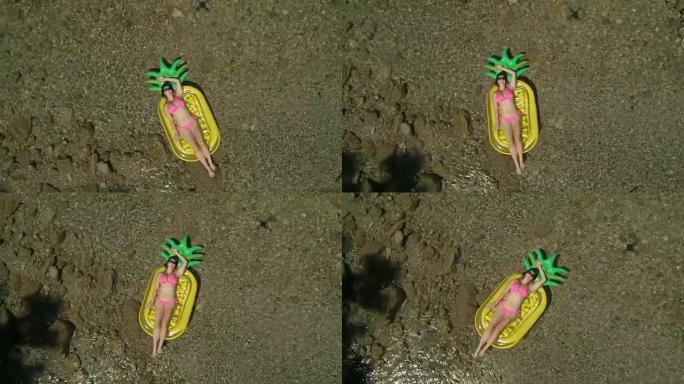 空中: 美丽的女人在菠萝形状的漂浮物上晒日光浴。