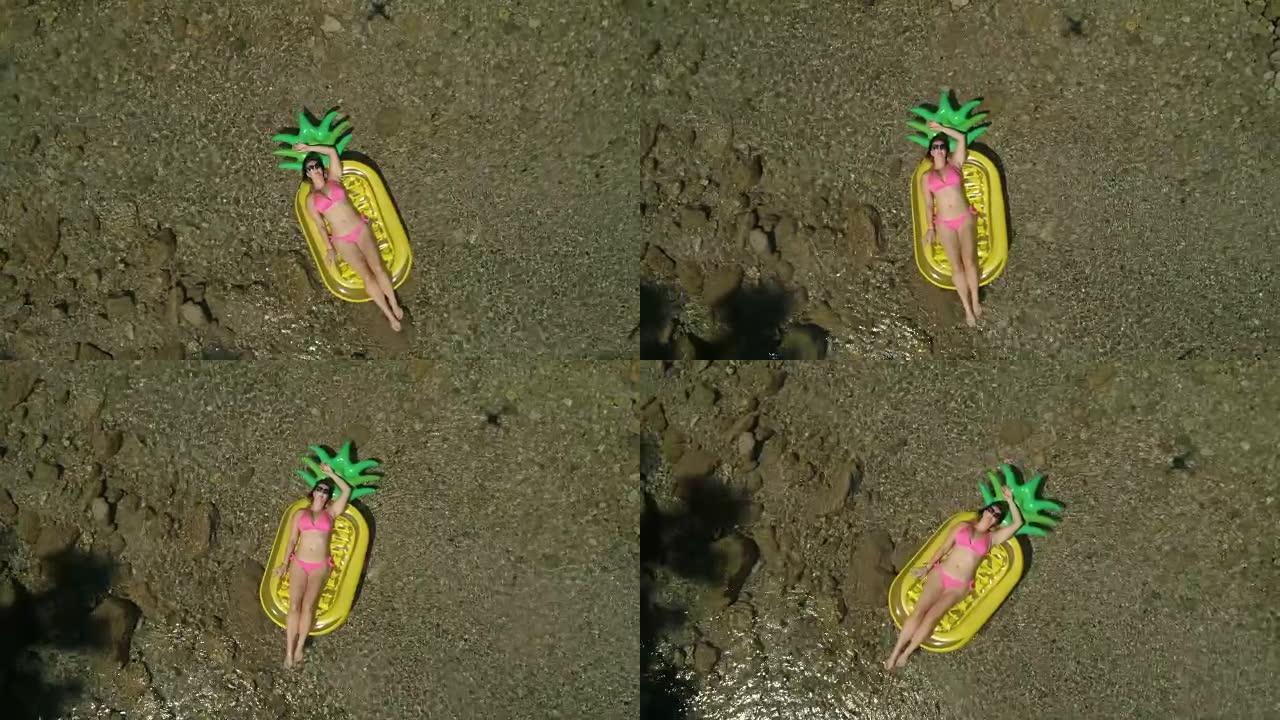 空中: 美丽的女人在菠萝形状的漂浮物上晒日光浴。