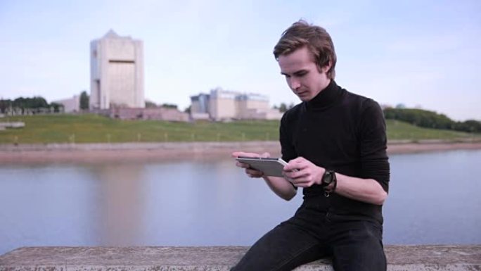 年轻人在城市湖附近的平板电脑上收到消息