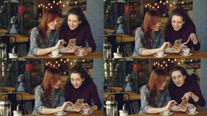 两个年轻漂亮的女友在咖啡馆里使用智能手机，在情感上大笑和交谈。社交媒体、会友与现代科技理念。