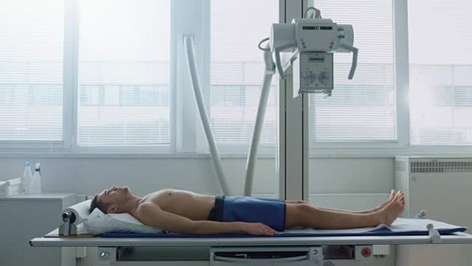 在医院里，一名男子坐在床上等待x光机扫描他的腿是否受伤。扫描骨折、四肢骨折、癌症或肿瘤。拥有技术先进